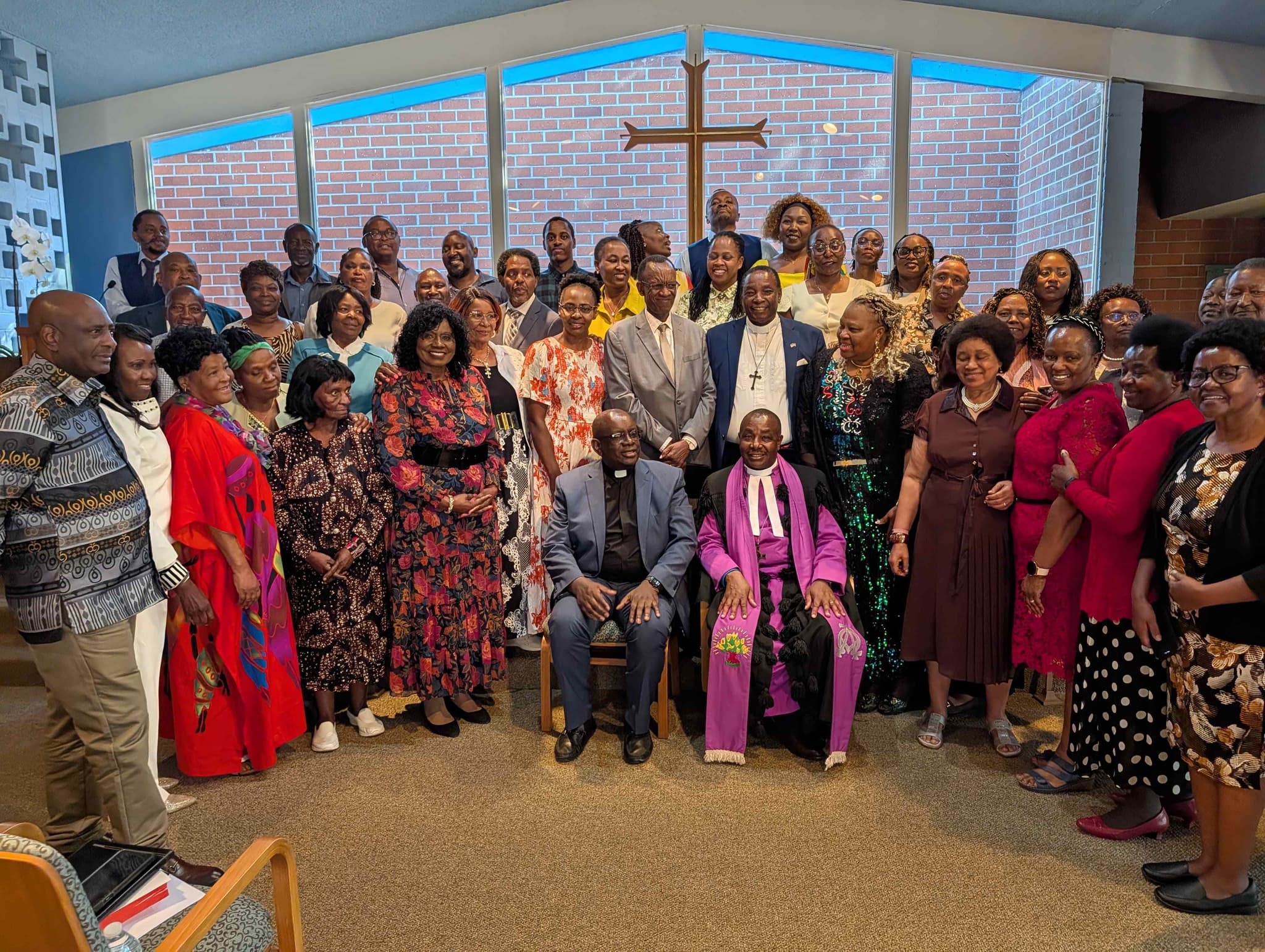 CAGI congregation gathered in worship, with church leaders seated in front and the community standing together beneath a wooden cross